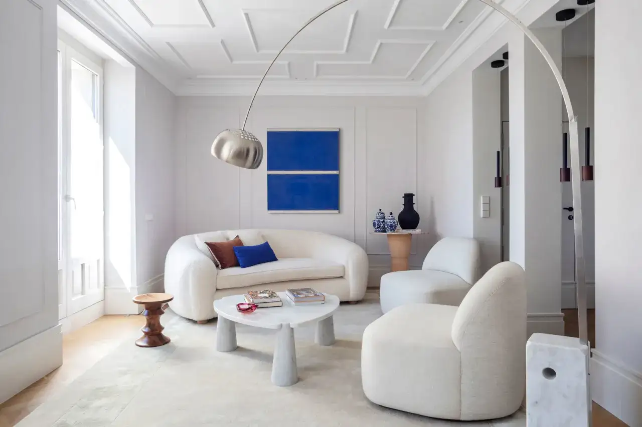 Sof&aacute; blanco curvo, mesa de centro de m&aacute;rmol y arte abstracto azul, ejemplos de las ultimas tendencias en decoracion de paredes.