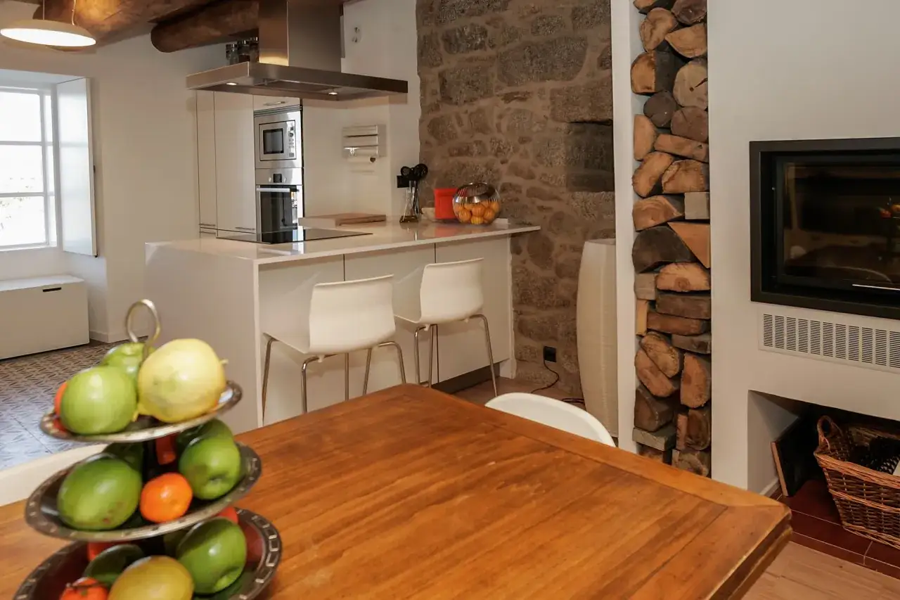 Cocinas con chimenea rústica y moderna. Barra de cocina blanca con taburetes, encimera de piedra y leña apilada junto a la chimenea.