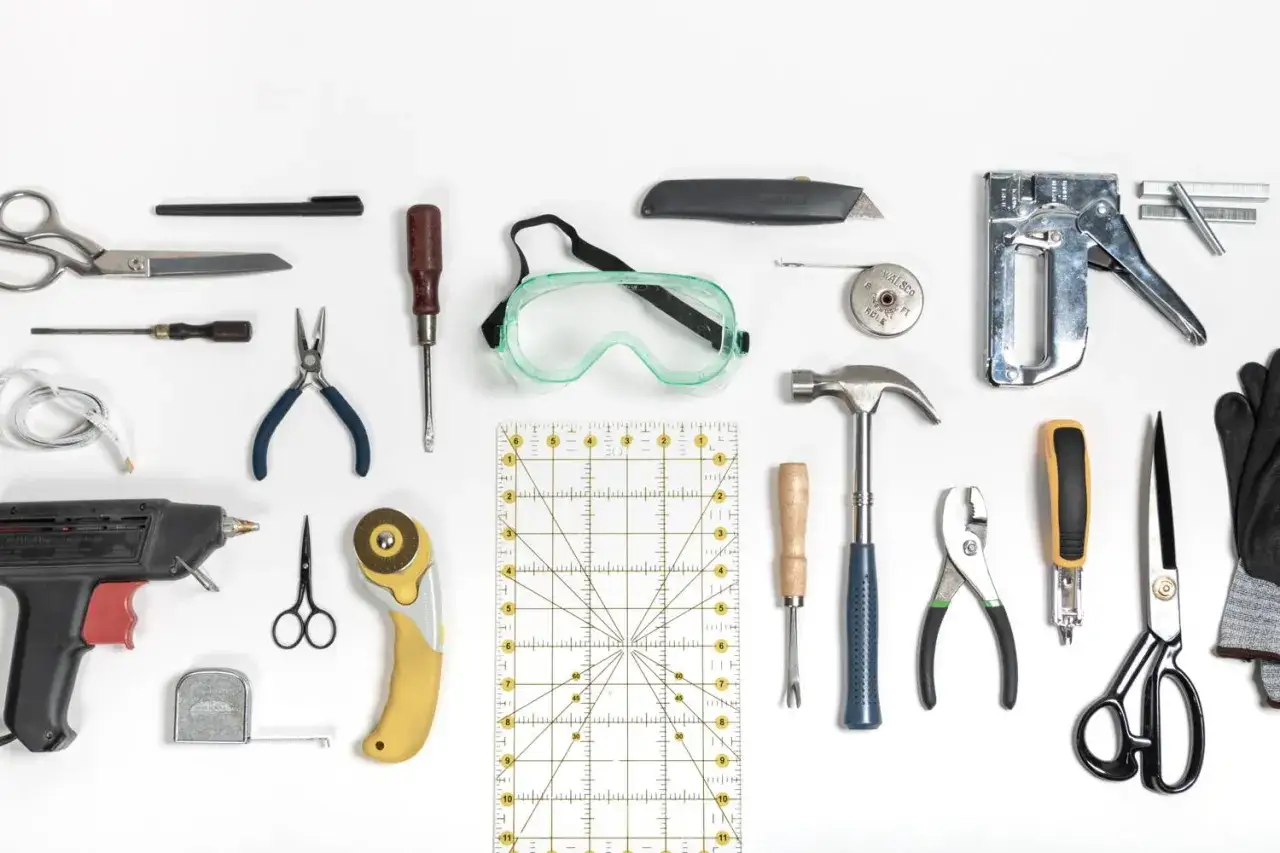 Herramientas para tapizar un sof&aacute;: tijeras, c&uacute;ter, grapadora, martillo, alicates, destornilladores, pistola de silicona, gafas de seguridad y cinta m&eacute;trica.