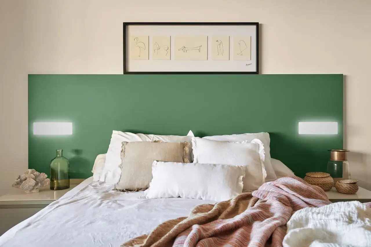 Cama con cabecero verde y cuadros de Picasso. La distancia entre interruptores cabecero cama es sim&eacute;trica, iluminando la estancia.
