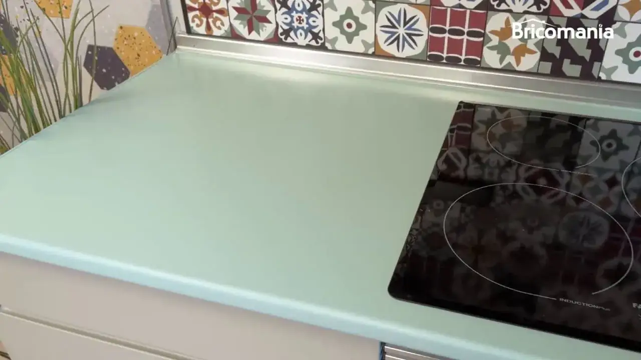 Encimera de cocina verde menta, con azulejos coloridos de estilo hidr&aacute;ulico detr&aacute;s. Una placa de inducci&oacute;n negra est&aacute; a la derecha.