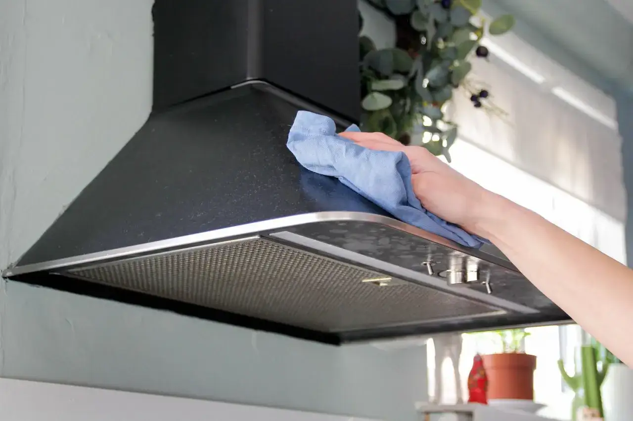 Mano limpiando el extractor de cocina con un paño azul.