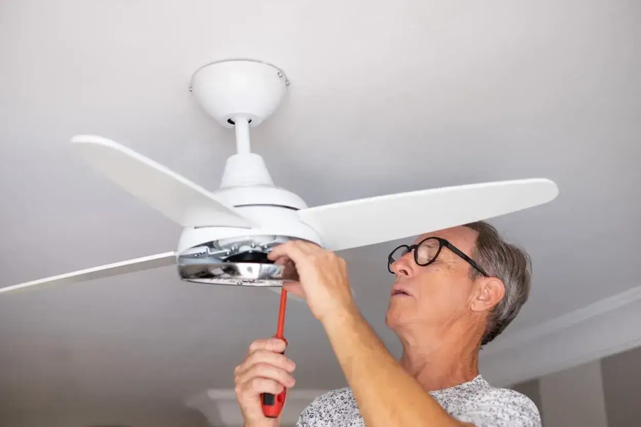 Hombre con gafas ajusta un ventilador de techo de pladur con un destornillador.