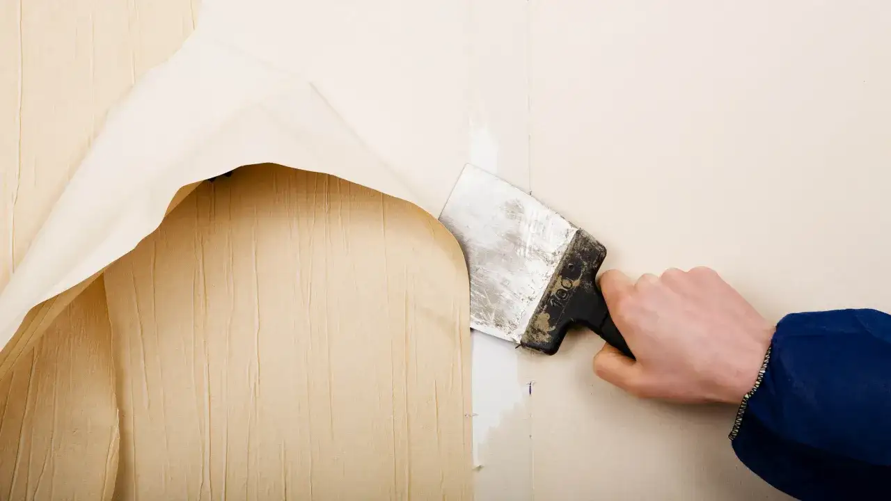 Mano con espátula quitando papel pintado viejo de una pared.