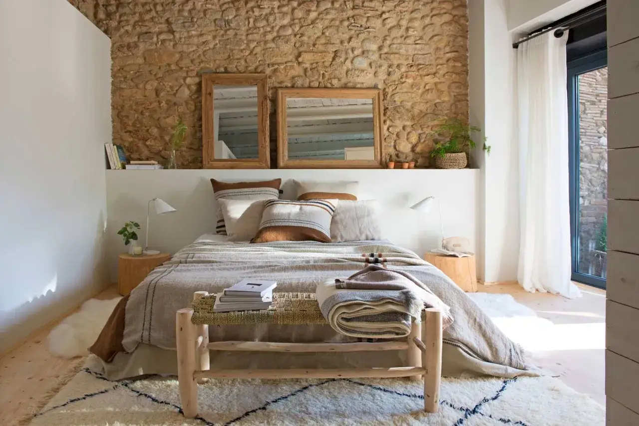 Ideas como decorar una habitaci&oacute;n de matrimonio moderna: cama con textiles c&aacute;lidos, pared de piedra r&uacute;stica, espejos de madera y alfombra acogedora.
