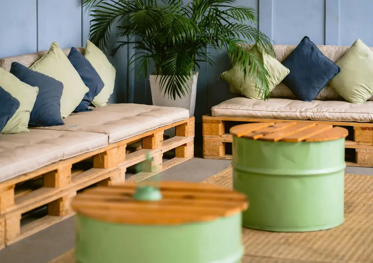 Sof&aacute;s y mesas bajas creados con decoraci&oacute;n con palets, complementados con cojines y plantas para un ambiente acogedor.
