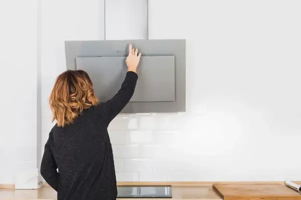 Mujer toca panel de control de campana extractora moderna, lista para cambiarla o limpiarla.