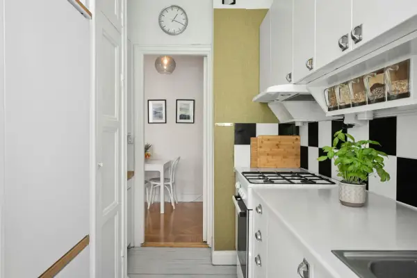 Cocina blanca y ordenada con estantes transparentes para organizar alimentos. Al fondo, un comedor pequeño.