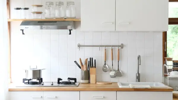 Una cocina pequeña y luminosa con encimera de madera, utensilios colgados y un fregadero.